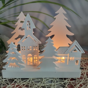 Puede incluir: Escena de pueblo navideño de madera blanca con una iglesia, casas y árboles. La escena está iluminada con luces blancas cálidas.