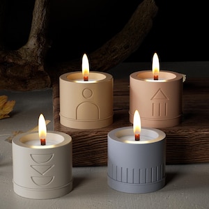 May include: Four small, cylindrical candles with different geometric designs and a warm, glowing light. The candles are made of concrete and have a natural, earthy aesthetic.