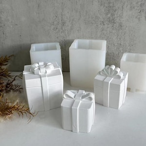 May include: White gift box moulds with bow details. The moulds are in various sizes and shapes, ideal for creating decorative gifts. The image shows several moulds, some with lids and others without, all in a clean, minimalist style.