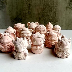 May include: A collection of 11 small, hand-painted ceramic figurines of various animals wearing knitted sweaters. The figurines are in shades of pink and white and are arranged on a white surface.