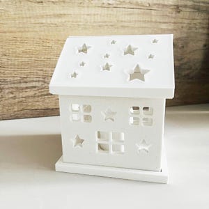 May include: White wooden house shaped candle holder with cut-out star and window designs.