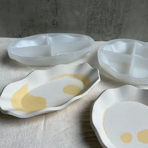 May include: Four white ceramic serving dishes with scalloped edges. Two of the dishes are divided into three sections. The other two dishes have a yellow glaze on the inside.