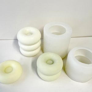 May include: Set of five white silicone molds for making candles. The molds are shaped like donuts with a hole in the center. Two of the molds are stacked on top of each other.