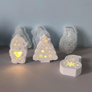以下が含まれることがあります： 白のクリスマスをテーマにしたLEDライト。ノーム、クリスマスツリー、雪だるまの形です。ライトは温かい光を放ち、ノームはハート型の切り抜きが特徴です。ツリーと雪だるまには星と雪の結晶のデザインがあります。