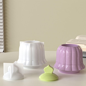 Puede incluir: Colección de objetos decorativos de cerámica en una paleta de colores pastel. Incluye un jarrón blanco acanalado, un jarrón color lavanda, un pequeño soporte blanco y una tapa verde lima. Los jarrones tienen forma de tulipán.