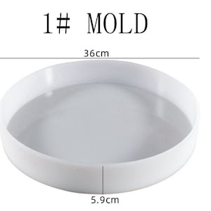 Könnte beinhalten: Weiße runde Plastikform, 36 cm im Durchmesser und 5,9 cm hoch. Die Form wird zum Herstellen von Bastelarbeiten oder anderen Projekten verwendet.