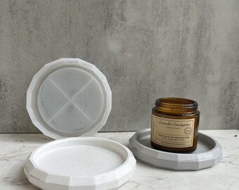 Può includere: Due portacandele in ceramica bianca, uno con un design geometrico e l'altro con una semplice forma rotonda. Un barattolo di candela in vetro marrone con un'etichetta che recita "Lavender Eucalyptus Soy Wax Candle Hand Poured" è appoggiato sul portacandele geometrico.