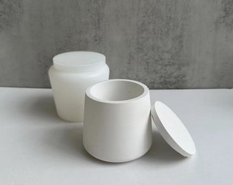 May include: Two white ceramic containers with lids. The container on the left is taller and rounder, while the container on the right is shorter and wider. Both containers have a smooth, matte finish.