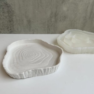 May include: Two white ceramic trays with a tree ring design. The trays are different sizes and have a rough, textured edge.