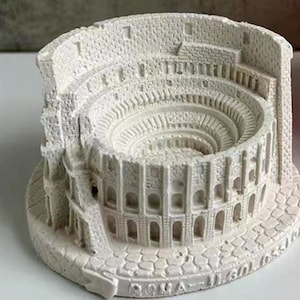 以下が含まれることがあります： ローマ、イタリアにあるコロッセオの白いセラミックモデル。モデルはアーチと柱で詳細に作られています。モデルのベースは、"ROMA"という文字が書かれたテクスチャ加工された表面です。