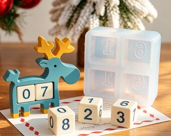 May include: A teal and yellow reindeer-shaped wooden perpetual calendar with two square blocks displaying the number 07, accompanied by three additional cream-colored number cubes and a translucent silicone mold with square cavities.