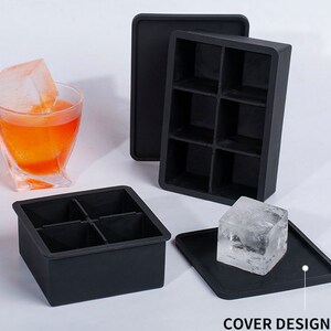 Pode incluir: Duas bandejas de cubos de gelo de silicone preto. Uma bandeja tem seis compartimentos e a outra tem quatro compartimentos. Um cubo de gelo transparente está sentado em uma tampa de silicone preta.