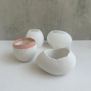 Può includere: Quattro vasi in ceramica bianca di forme diverse. Un vaso ha un bordo rosa. I vasi sono perfetti per piccole piante o piante grasse.