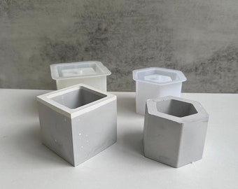 May include: Four concrete planters, two square and two hexagonal, with a white interior. The planters are made of a light gray concrete and are perfect for small plants or succulents.