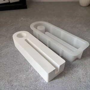 May include: Two white silicone moulds for making concrete or resin crafts. The moulds are designed to create a rectangular shape with a circular cutout and a slot in the centre.