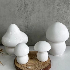 May include: Four white ceramic mushroom figurines of varying sizes. The largest mushroom has a dotted pattern. The mushrooms are arranged on a wooden base.