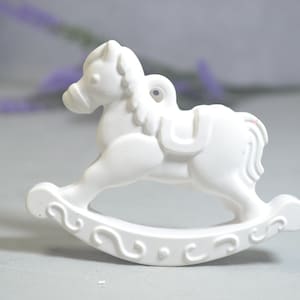 Puede incluir: Adorno de caballo de balancín de cerámica blanca con una silla de montar y un agujero para colgar.