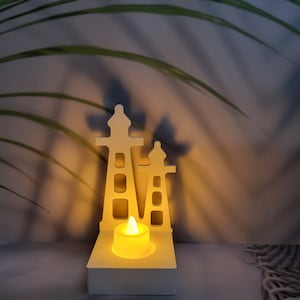 Puede incluir: Portavelas de madera blanco en forma de dos faros con una sola vela de té en el centro.