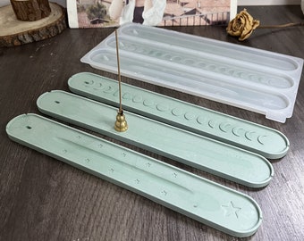 May include: Three green ceramic incense holders with a crescent moon design. The holders are arranged in a stack, with the largest at the bottom and the smallest at the top. A brass incense burner sits on top of the holders.