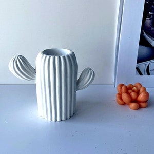May include: White ceramic cactus planter with a ribbed texture and two arms. The planter is sitting on a white surface.