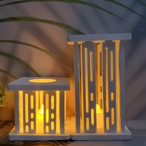 Puede incluir: Dos portavelas de madera blanca con diseños geométricos. Los portavelas están iluminados con velas votivas, proyectando un cálido resplandor.