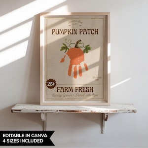 以下が含まれることがあります： 明るい茶色の背景に、手形のかぼちゃのデザインが施された額入りのプリント。テキスト「Pumpkin Patch」はカボチャの上に、「Farm Fresh」は下にあります。プリントは白い棚に飾られています。
