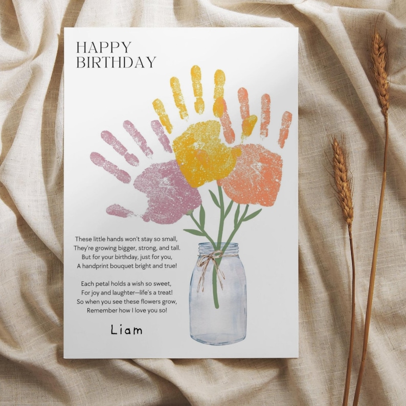 May include: A white birthday card featuring the text HAPPY BIRTHDAY and a poem about handprints. The design shows a clear glass mason jar with green stems topped by three colorful handprint flowers in yellow, orange, and purple. The name Liam is printed at the bottom.