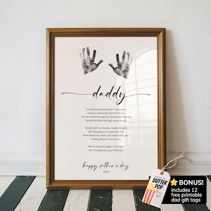 May include: A framed print featuring two black ink handprints at the top, the word daddy in script, a poem about fatherhood, and the text happy father's day 2026. A small gift tag with the text BONUS Includes 12 free printable dad gift tags.