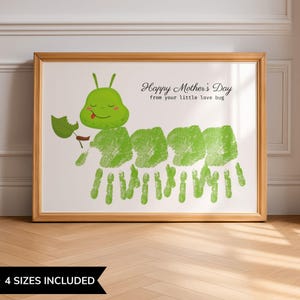 Op de afbeelding: Een ingelijste print met een groen rupsontwerp gemaakt van hand- en voetafdrukken. De rups houdt een blad vast en de tekst luidt "Happy Mother's Day from your little love bug". De lijst is lichtbruin.