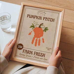 Könnte beinhalten: Ein gerahmter Druck mit hellbraunem Hintergrund zeigt ein Kürbisdesign mit Handabdruck. Der Text lautet "Pumpkin Patch" und "Farm Fresh". Der Rahmen besteht aus hellem Holz. Der Druck enthält auch den Text "Autumn's Best" und "Locally Grown - Picked with Love."