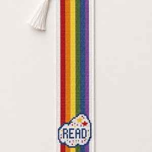 May include: A rectangular cross-stitch bookmark featuring vertical stripes in red, orange, yellow, green, blue, and purple. A white cloud-shaped motif at the bottom contains the word READ in blue letters, surrounded by small colorful star accents.