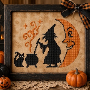 Peut inclure: Une broderie au point de croix encadrée sur tissu beige représentant la silhouette noire d'une sorcière remuant un chaudron avec un chat noir, devant un grand croissant de lune orange avec un visage, ornée d'un nœud à carreaux noir et orange.