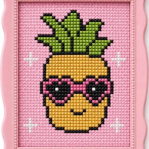 Puede incluir: Un bordado de punto de cruz de una piña con gafas de sol rosas en forma de corazón, sobre un fondo rosa. La obra enmarcada presenta un borde rosa con un detalle de corazón en la parte superior. Estrellas blancas en las esquinas.