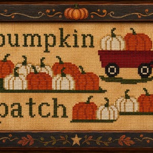 Może przedstawiać: Oprawiony haft krzyżykowy z napisem "pumpkin patch" ciemnozielonymi literami. Wzór zawiera pomarańczowe i białe dynie, czerwony wózek oraz ciemnobrązową ramę ozdobioną namalowanymi jesiennymi liśćmi i gwiazdą.