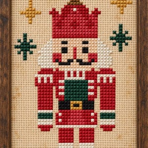 May include: A framed cross-stitch embroidery featuring a nutcracker figure in a red, green, and black uniform with a tall hat. The design is set against a beige fabric background and is surrounded by small, embroidered gold and green star shapes.