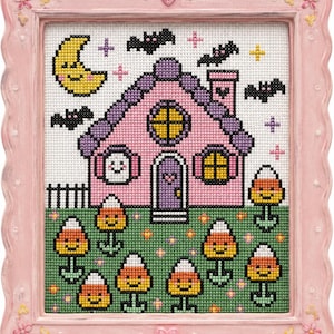 Puede incluir: Un punto de cruz enmarcado con una casa rosa con techo morado, una luna sonriente y murciélagos. La casa tiene un fantasma sonriente en la ventana y flores de maíz dulce en el jardín. El marco rosa tiene corazones y flores decorativas.