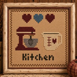 May include: A framed cross-stitch embroidery on tan fabric featuring a dark red stand mixer, a light blue heart between two dark red hearts, a cream-colored measuring cup with a small red heart, and the word Kitchen in black block letters.
