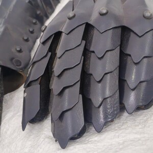 May include: A pair of black leather gauntlets with metal scales. The gauntlets are designed to protect the hands and fingers.