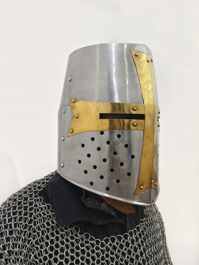 May include: A silver helmet with a gold cross on the front. The helmet has a visor and is decorated with small rivets. The helmet is worn by a person wearing chainmail.