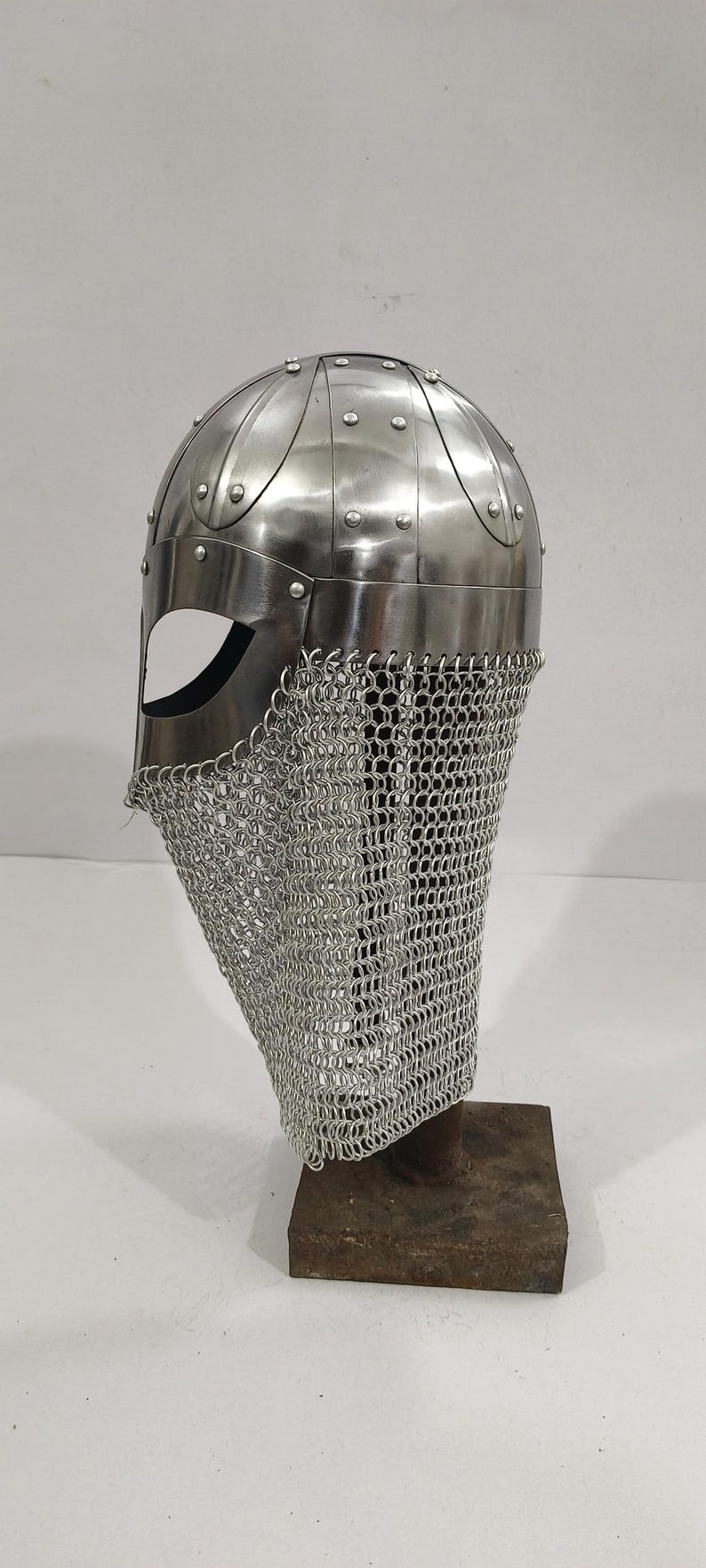 May include: A silver Viking helmet with a chainmail face mask. The helmet is on a wooden stand.