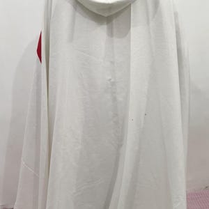 Op de afbeelding: Een witte gekapte robe met een rode bies aan de schouders. De robe is gemaakt van een zachte, vloeiende stof.
