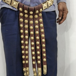 May include: A brown leather belt with gold metal accents and multiple straps hanging down. The belt is decorated with round, gold metal studs.