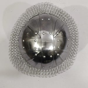 May include: A silver helmet with a chainmail coif. The helmet has a rounded dome shape with a series of raised ridges and rivets.