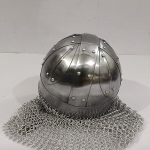 May include: A silver helmet with a chainmail coif. The helmet is made of metal plates and has a rounded shape. The chainmail coif is made of small metal rings.