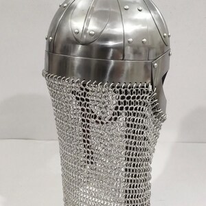 May include: A silver Viking helmet with a chainmail face mask, displayed on a wooden stand.