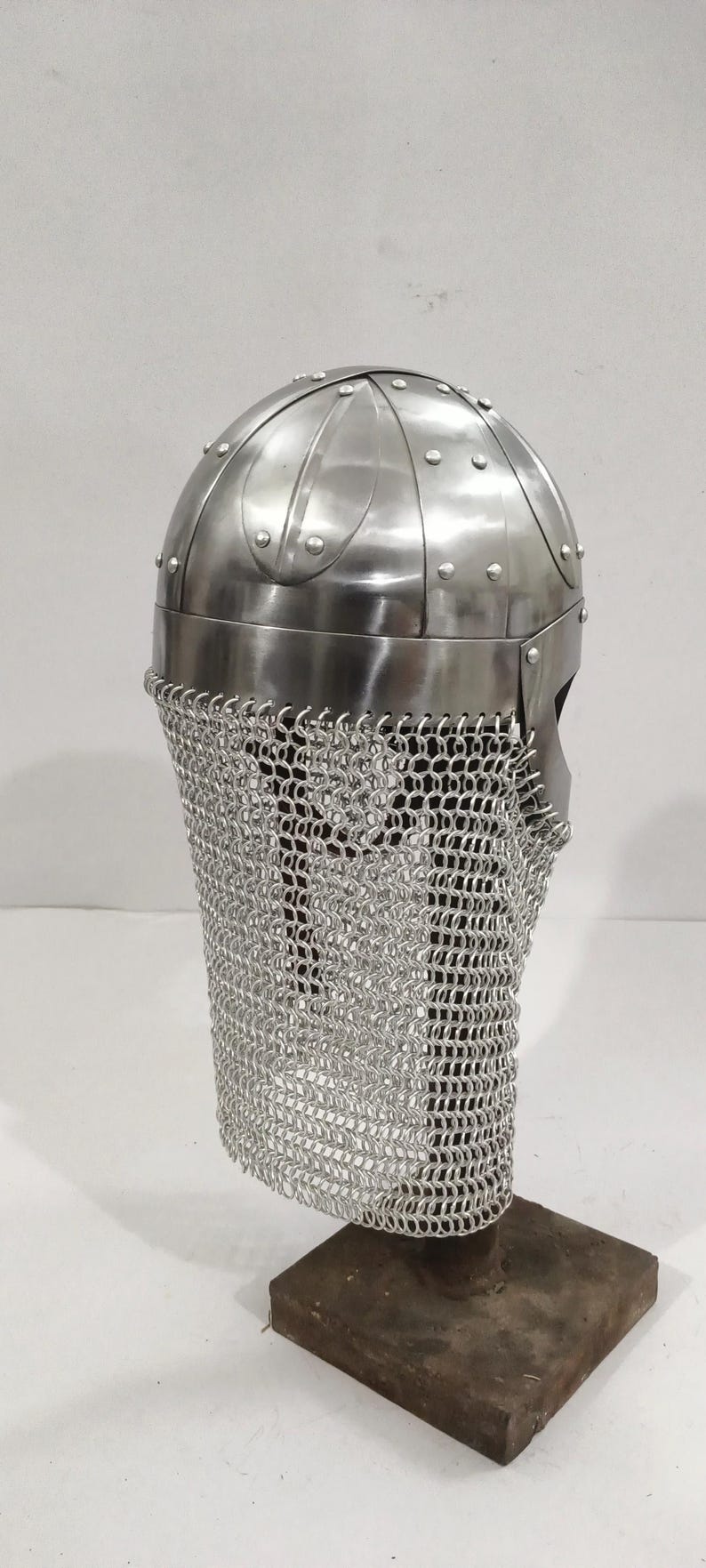 May include: A silver Viking helmet with a chainmail face mask, displayed on a wooden stand.