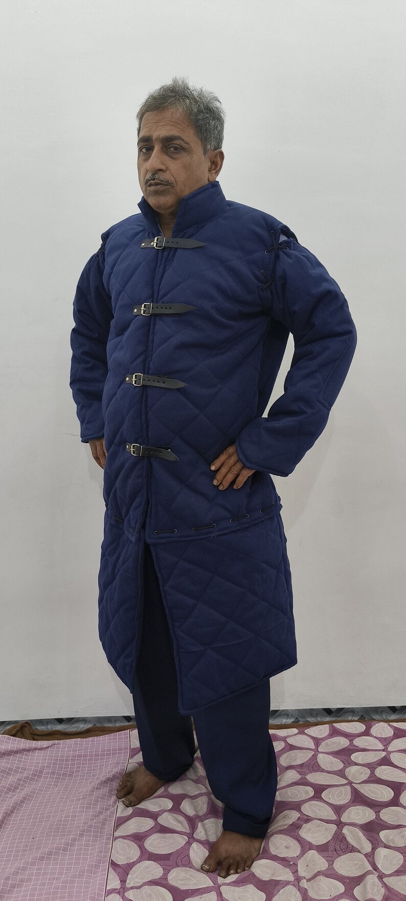 May include: A blue quilted jacket with a high collar and multiple buckles. The jacket has a diamond pattern and is lined with a soft material.