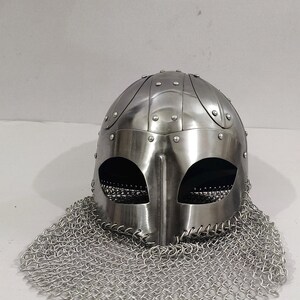 May include: A silver helmet with a chainmail coif. The helmet has a rounded top with a series of raised ridges and is decorated with rivets. The chainmail coif is made of small metal rings linked together.