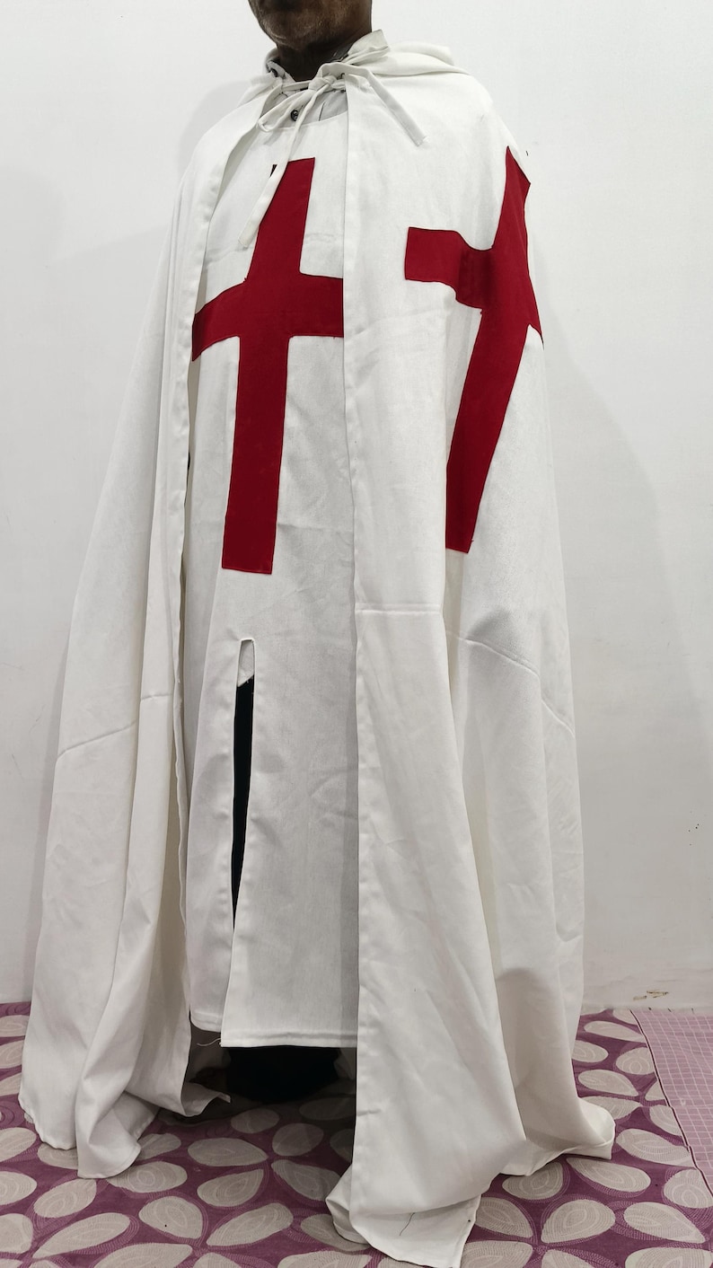 Op de afbeelding: Een witte kapmantel met een rood kruis op de voorkant. De mantel is gemaakt van een zachte, lichte stof en heeft een lang, vloeiend ontwerp.