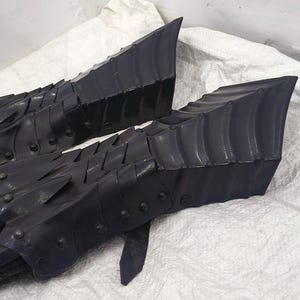 May include: A pair of black leather gauntlets with a scaly, armored design. The gauntlets are made of overlapping plates that create a textured surface.